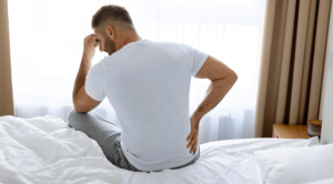 man waking up in bed hold his back in pain