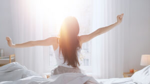 young woman waking up refreshed looking out at the morning sun